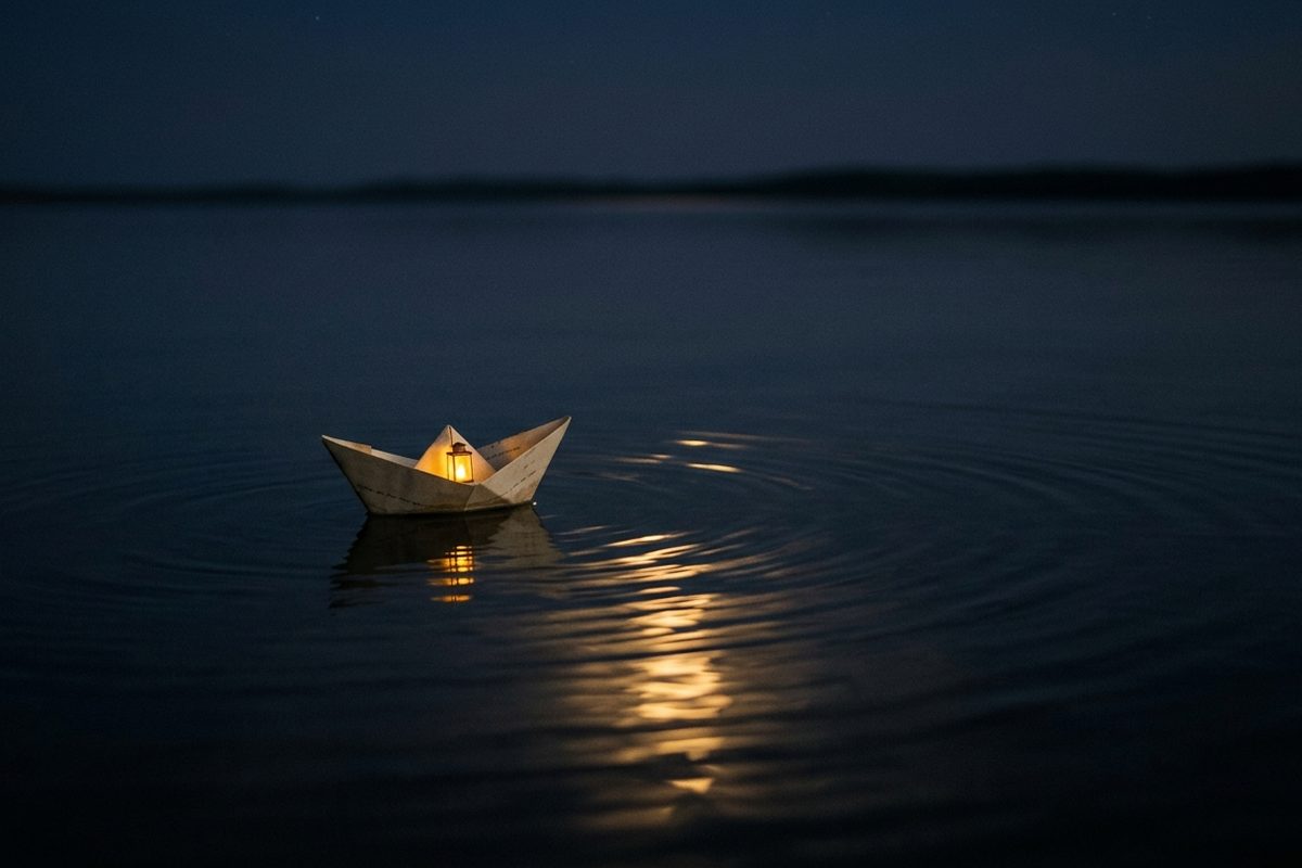 Perahu kertas kecil mengapung di air malam yang tenang dengan satu pantulan lampu keemasan